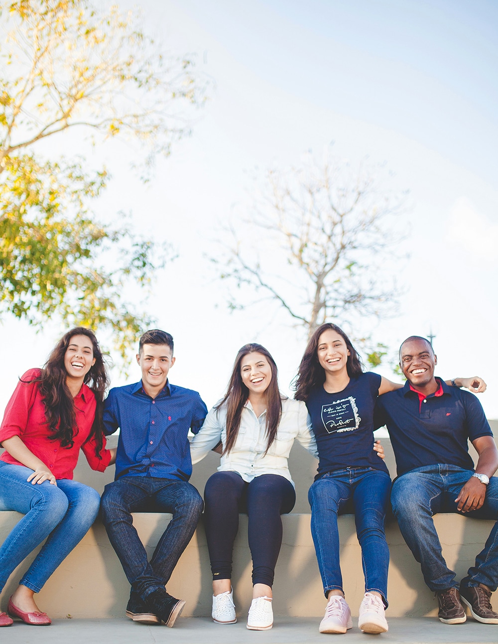 Group of teens and young adults arm in arm smiling outside